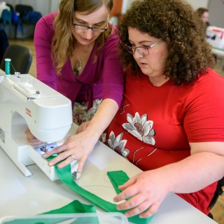 Warsztaty krawieckie w Centrum Sztuki Mościce - Dwie kobiety pracują przy maszynie do szycia trzymając w dłoni zielony materiał. - Fot : Przemysław Sroka