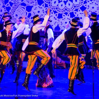 "Matulu, wyjrzyj na próg chaty" - występ Małych Świerczkowiaków - Mężczyźni w kolorowych strojach ludowych z czarnymi kapeluszami na głowach tańczą w kole, podskakując i unosząc ręce. - Fot. : Przemysław Sroka