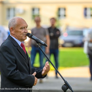 Urodziny Mościc - Mężczyzna mówi do mikrofonu, za nim w tle grupa ludzi stoi na trawie.  - Fot. Przemysław Sroka i Michał Żurowski